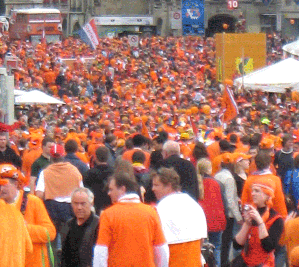 A crowd of Dutch (Netherlands, Holland) people wearing orange clothes and hats with flags
