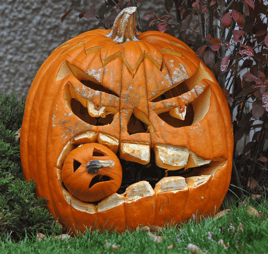 A scary pumpkin face eating a smaller pumpkin on a front lawn